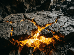 Cracked dark volcanic rocks with glowing orange molten lava visible in the fissures